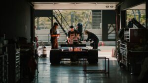 Formula-style racing car inside a motorsport garage with technicians working around the vehicle
