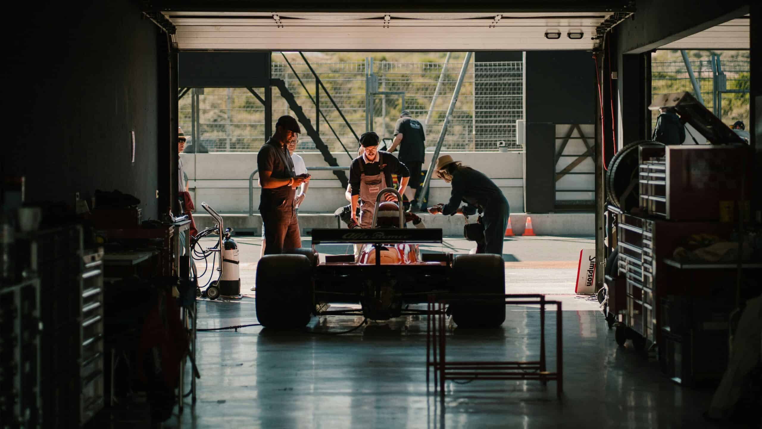 Formula-style racing car inside a motorsport garage with technicians working around the vehicle